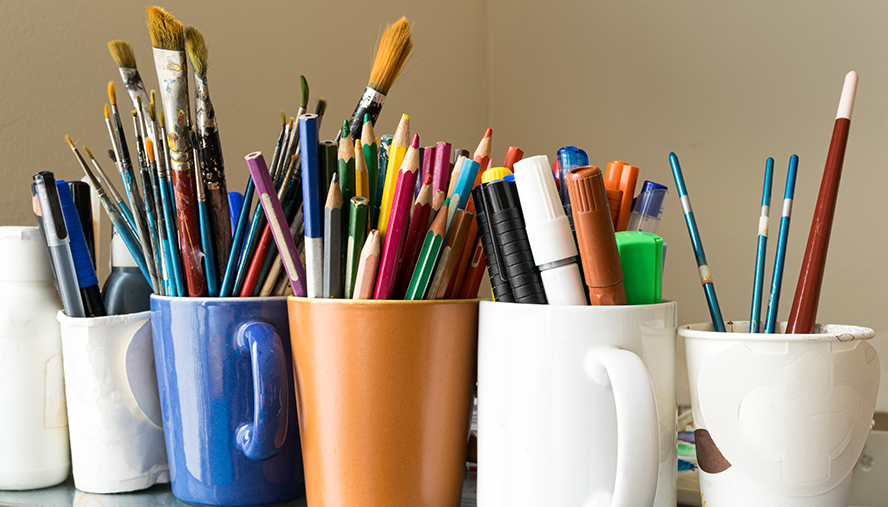 Mugs filled with colored pencils, markers, crayons, and paint brushes
